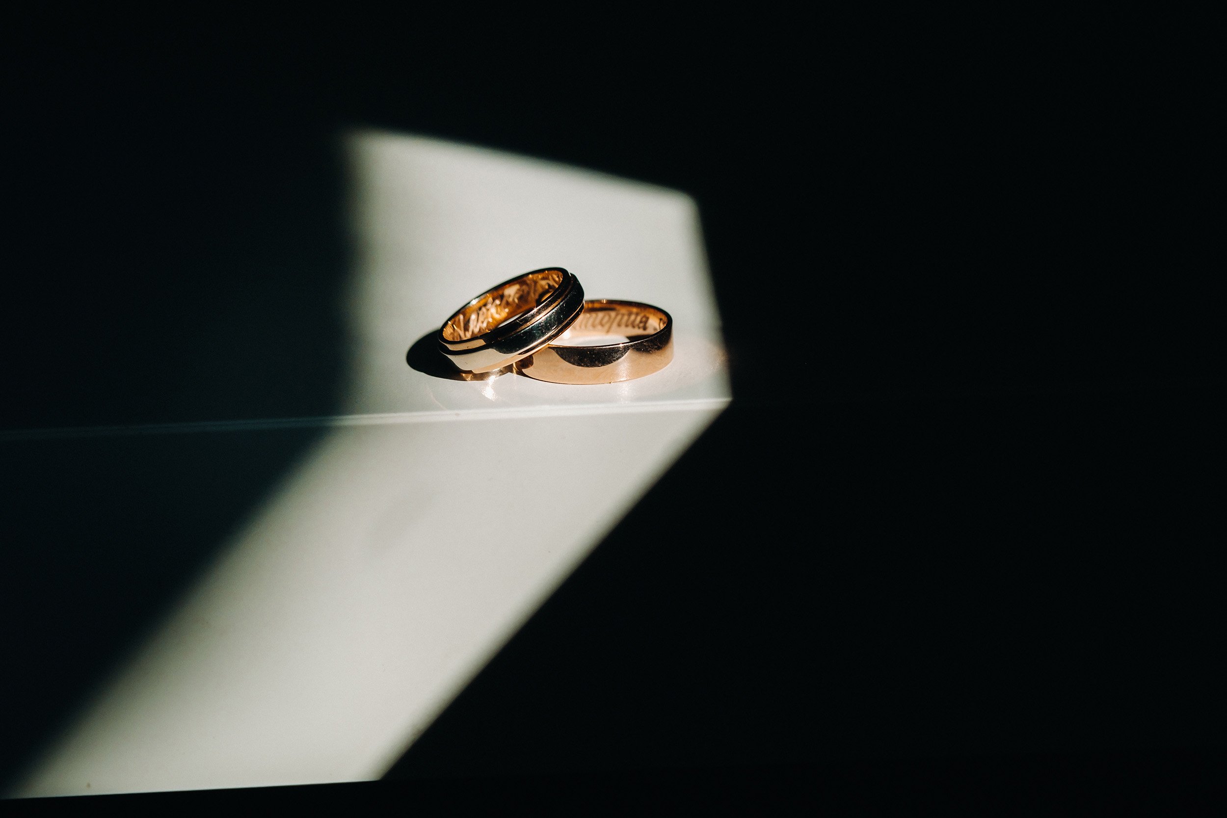 Two gold wedding rings placed on a white surface with a dramatic shadow, lit by a single light source.