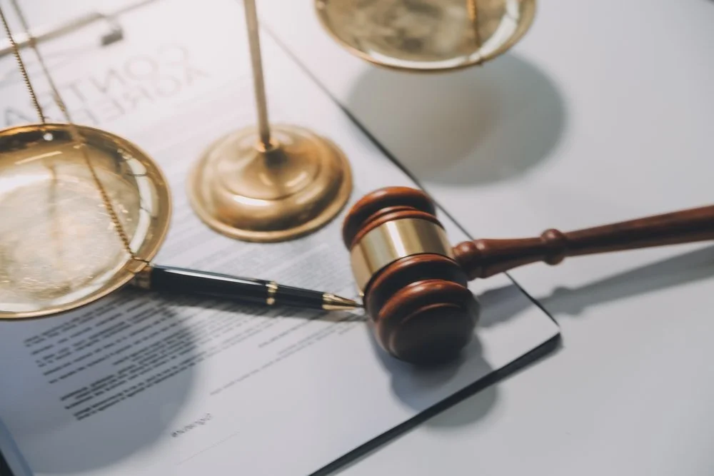 A judge's gavel resting on a legal document, with golden balance scales and a pen nearby.