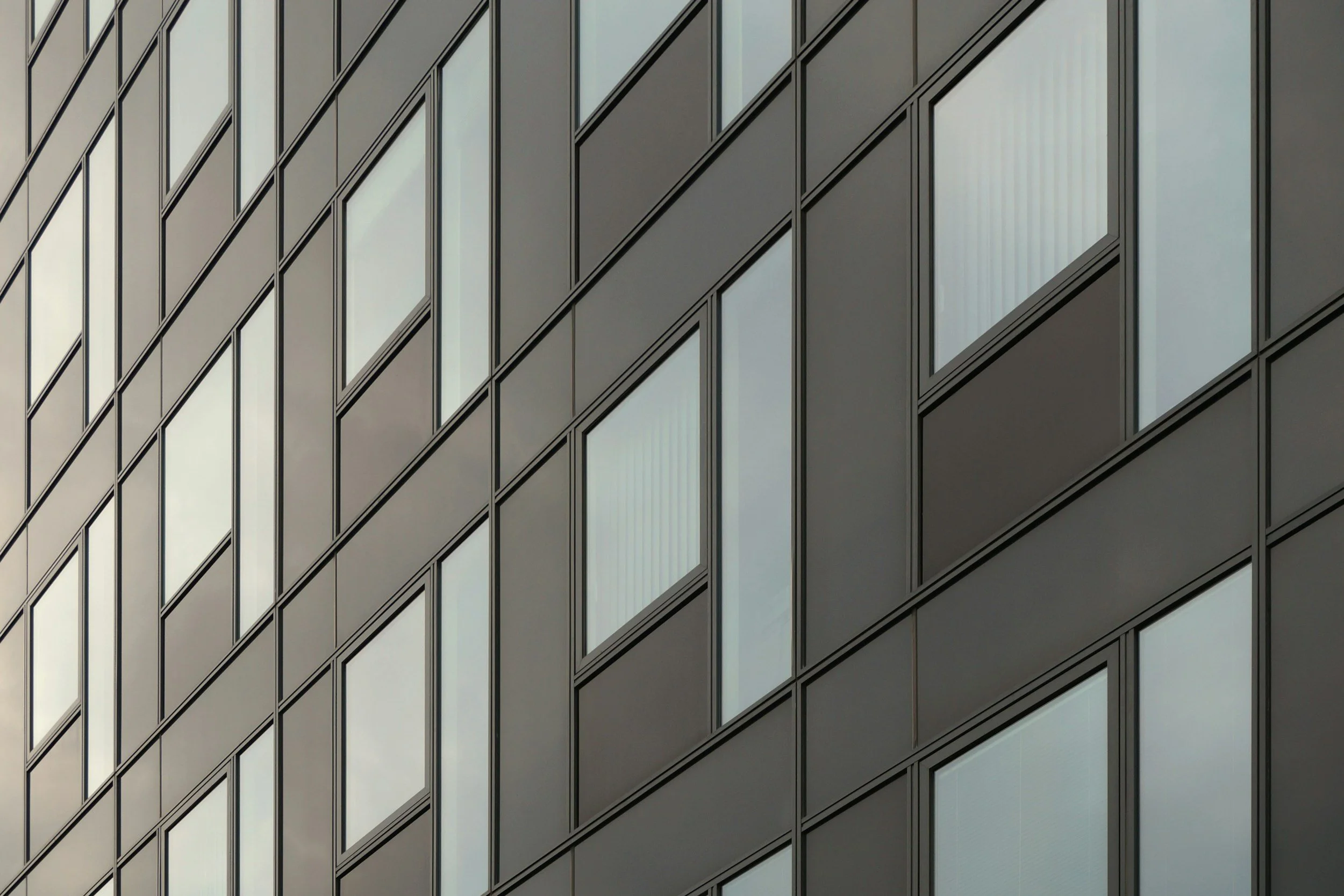 Close-up of a modern building's exterior with glass and metal panels arranged in a diagonal pattern.