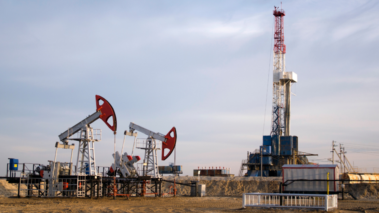 Active pump jacks and a tall drilling rig operating on an upstream production site managed by turn-key oilfield workforce solutions.