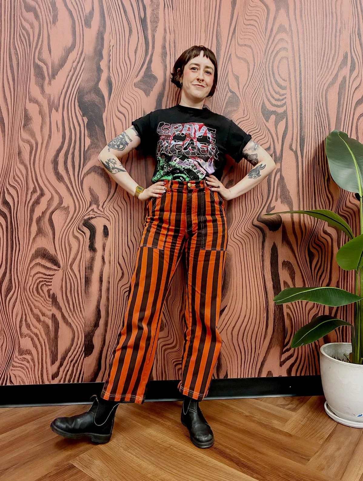 Molly Sparrow, haircutting specialist, with a short bob and micro bangs, posing against a wood grain wall at The Darling