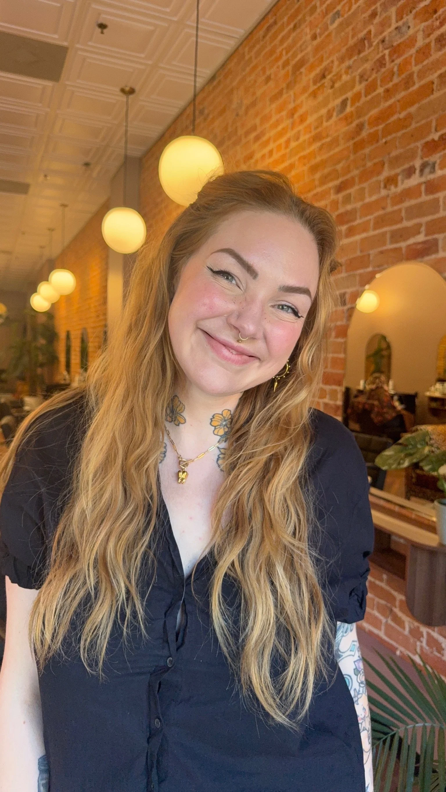 Kathryn Hills, lead stylist and color educator, with long golden blonde waves in front of the brick wall at The Darling