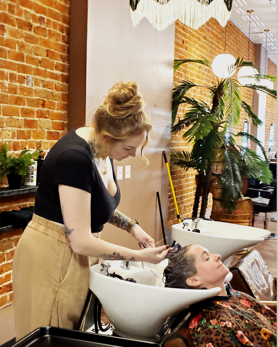 Hairstylist washing a client's hair at a salon shampoo station.