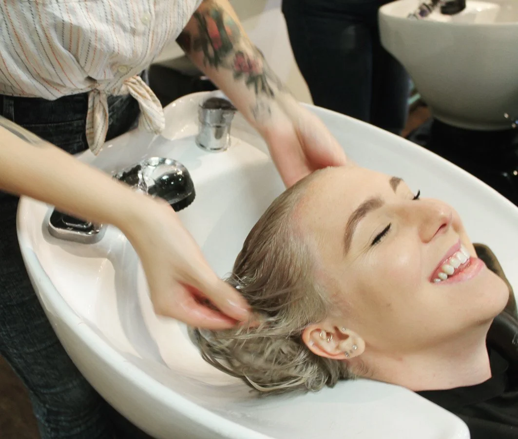 Hairdresser washing a smiling client's hair at a salon shampoo basin