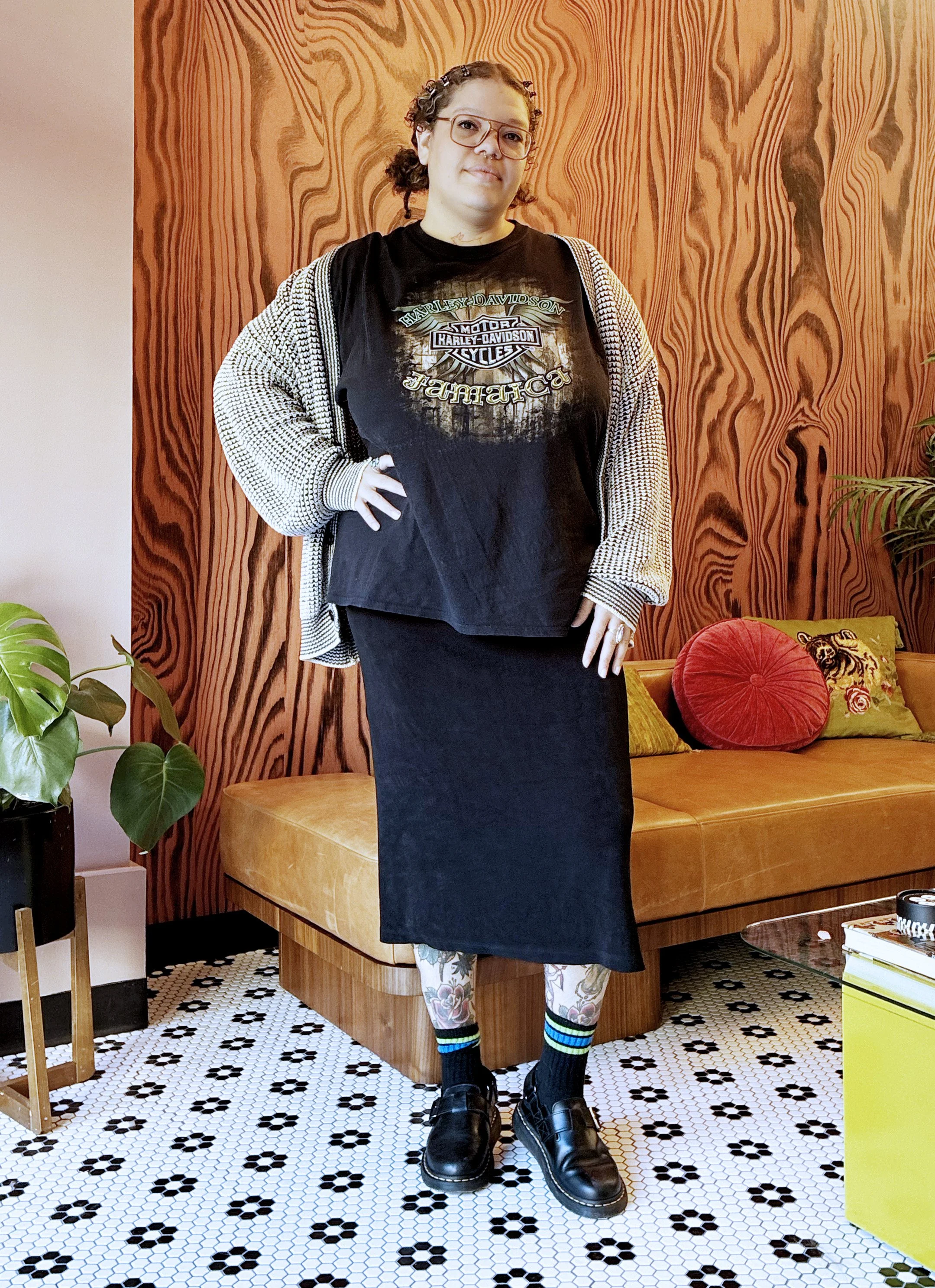 Sage Lowery, stylist for curls, razor cuts and balayage, with curls pinned back in clips and glasses, standing in the lounge at The Darling