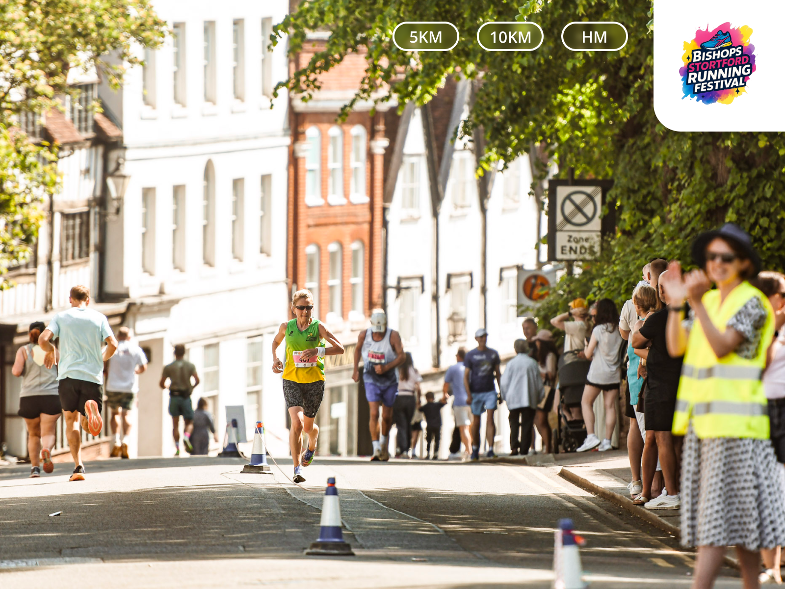 A group of runners participating in a race on a city street, with spectators on the sidewalks and historic buildings in the background.