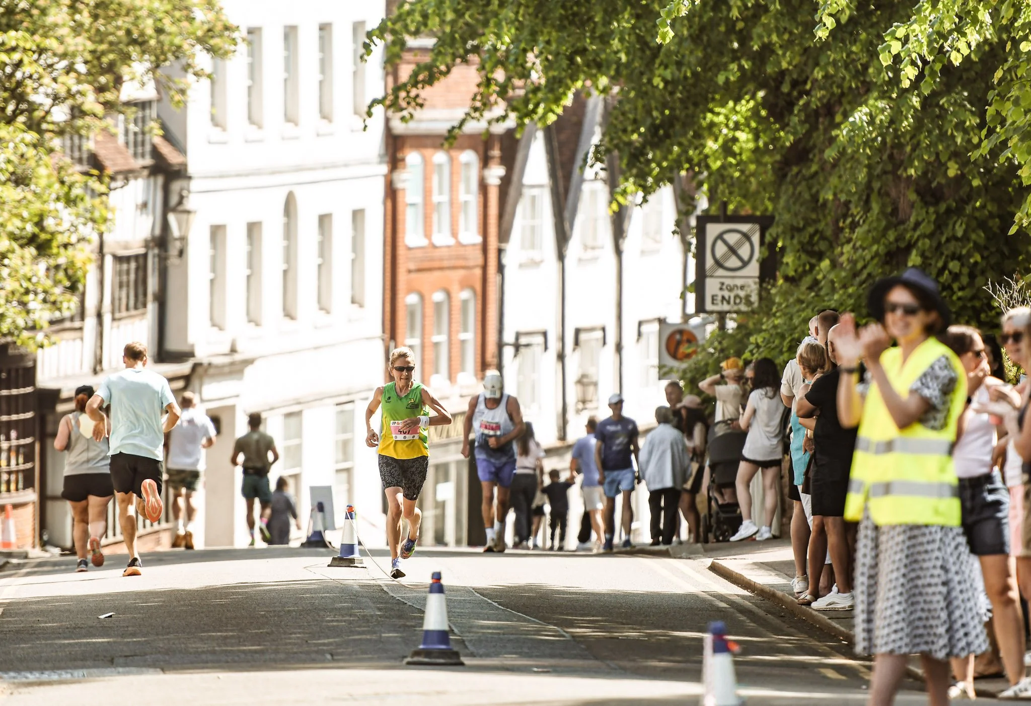 A group of runners participating in a race on a city street, with spectators on the sidewalks and historic buildings in the background.