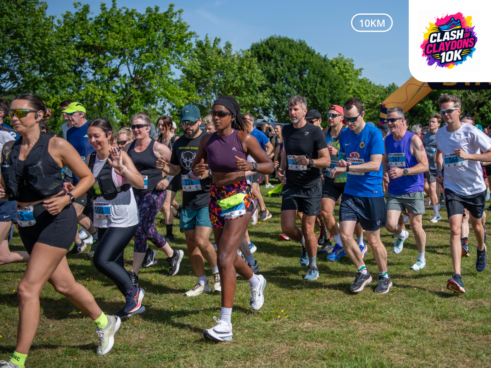 Group of people participating in a running race outdoors on a sunny day, with trees and a start arch in the background.