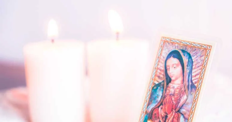 Two lit candles with a religious image of the Virgin Mary next to them.