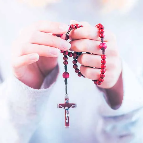 Person holding a red beaded rosary with a crucifix