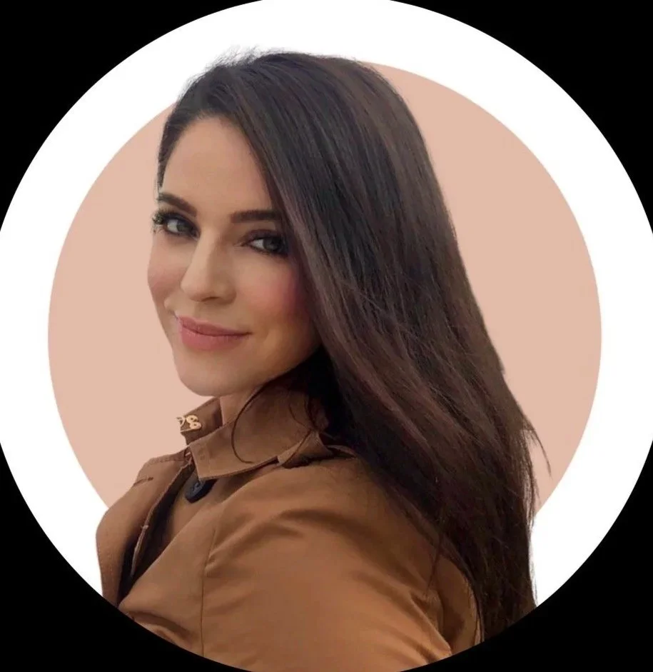 A woman with long dark hair smiling and looking at the camera, wearing a brown jacket, with a circular background that is light peach inside a black border.