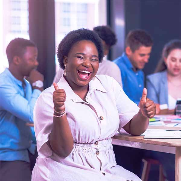 Happy woman giving two thumbs up in a group setting with others in the background.