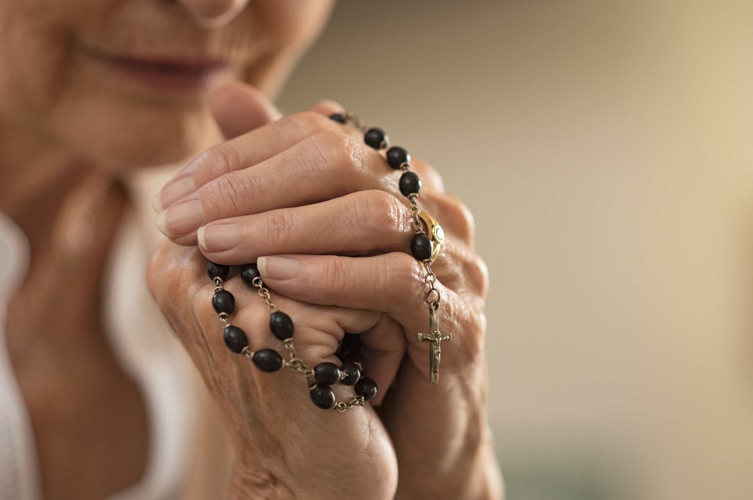 Close-up of a person's hands holding a rosary with black beads and a silver crucifix, with part of their face and mouth visible in the background.