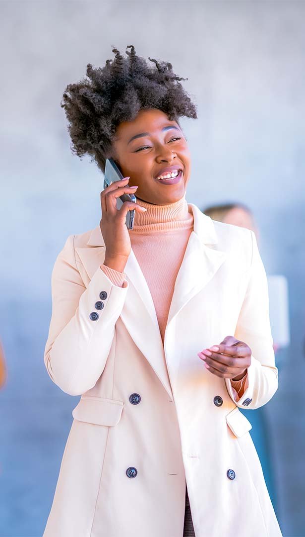 A smiling woman with natural curly hair talking on a mobile phone.