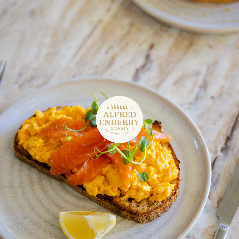 Scrambled eggs with smoked salmon on toast, garnished with microgreens and a lemon wedge on a white plate.