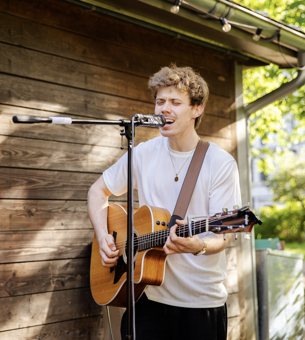 Young man singing into a microphone while playing an acoustic guitar outdoors.