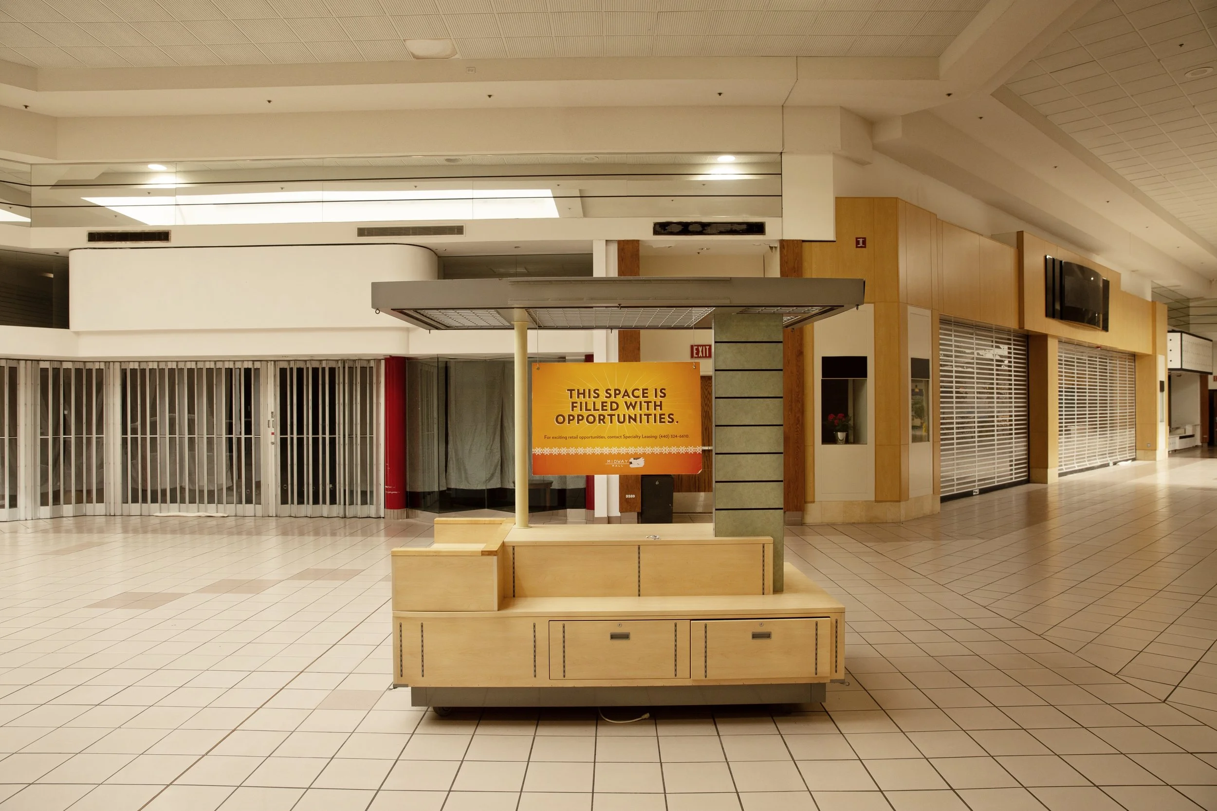 Empty shopping mall corridor with closed stores, cleaning cart in foreground, and sign reading "This space is filled with opportunities."