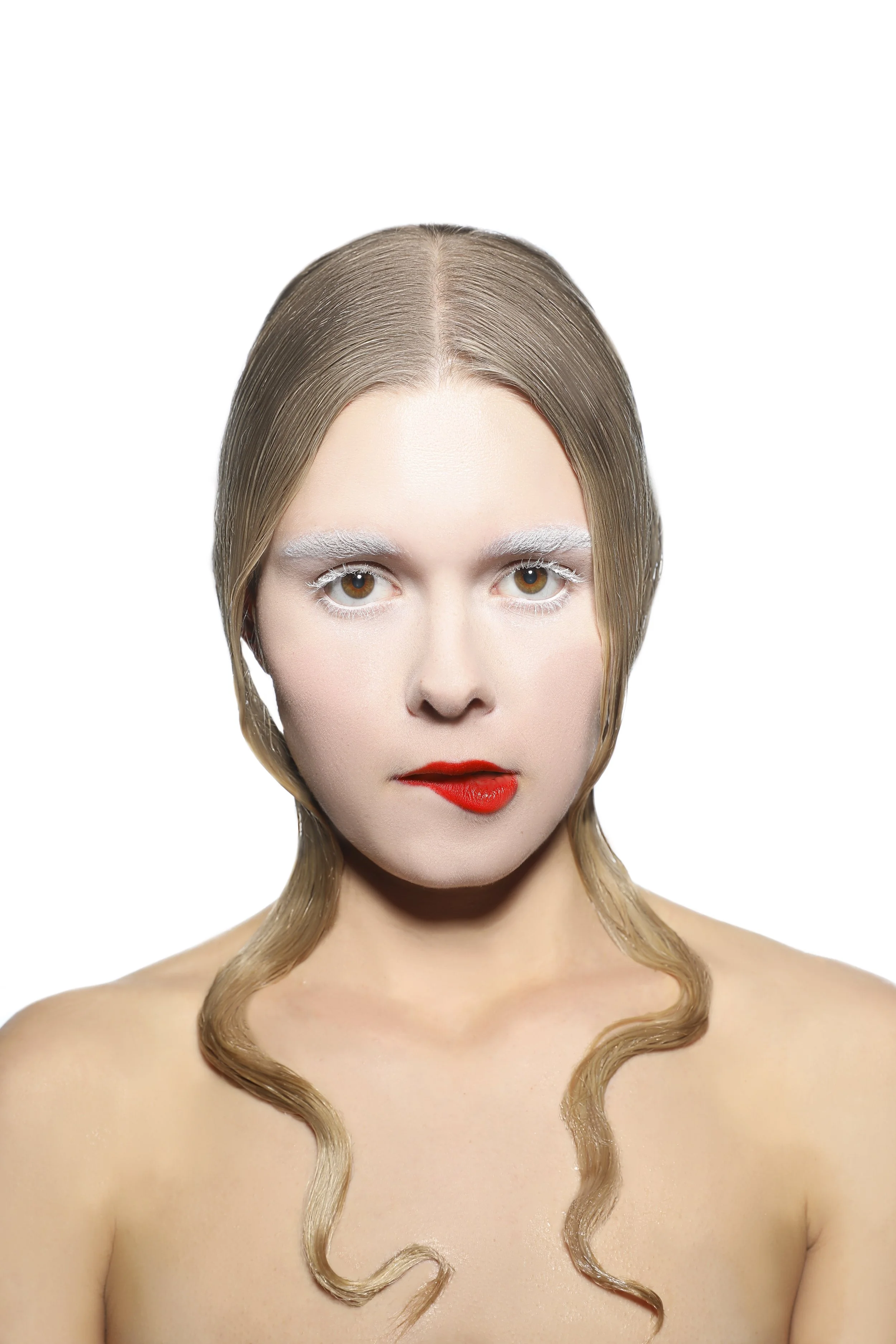 A woman with blonde hair styled with two long, loose curls framing her shoulders, red lipstick, and white eye makeup, looking directly at the camera against a white background.