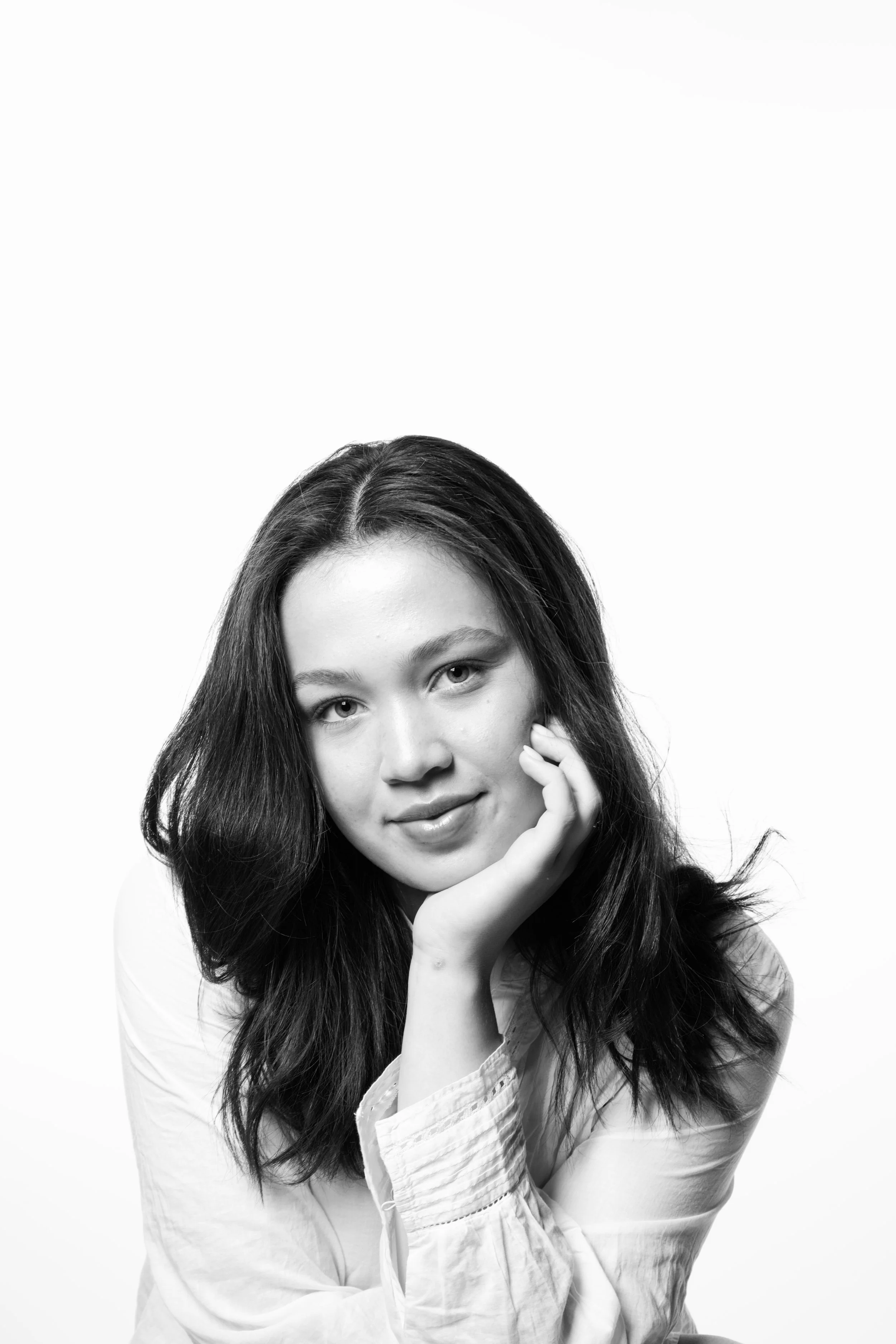 Black and white portrait of a young woman with long hair, smiling gently, resting her chin on her hand, wearing a button-up shirt.