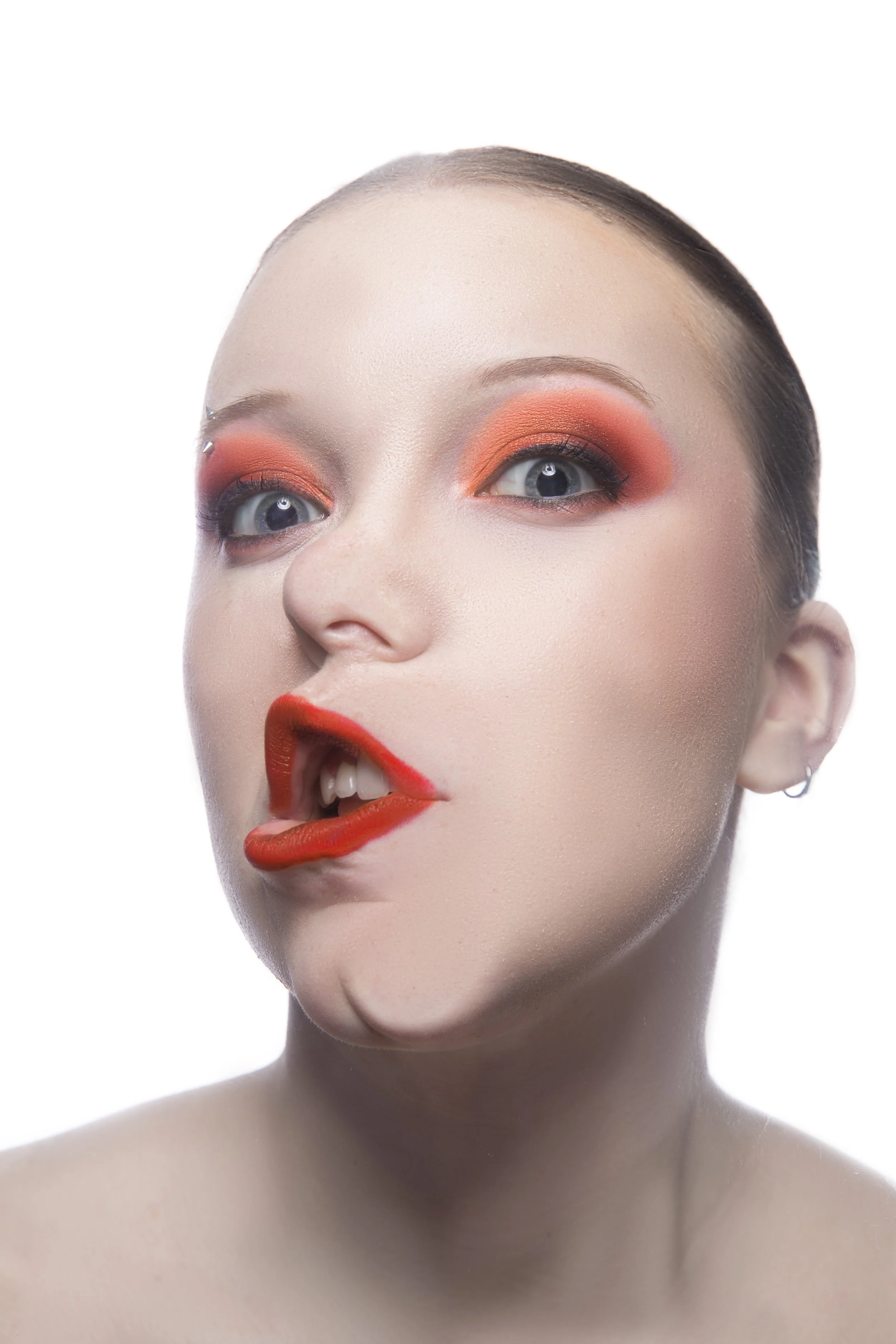 Close-up of a woman's face with artistic makeup, including orange eyeshadow, red lipstick, and a light complexion against a white background.