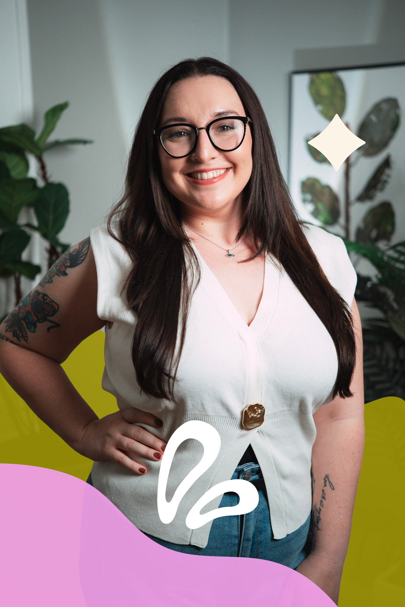 A smiling woman with long dark hair, glasses, and tattoos on her arms stands in front of a colorful backdrop with yellow and pink shapes, a window, and green plants.