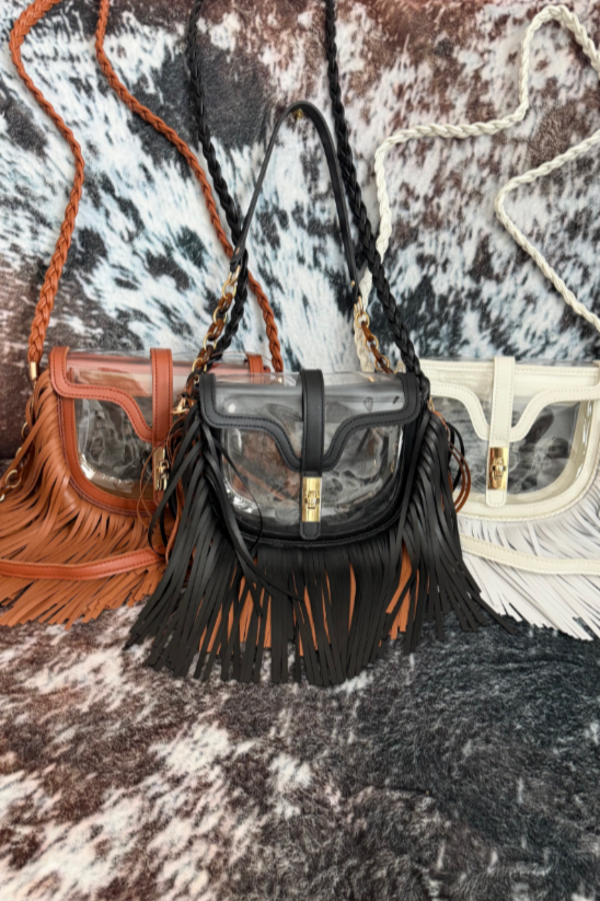 Clear concert venue bag with fringes, one in brown, one in black, and one in white, displayed on a patterned fabric background.