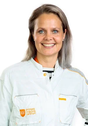 A woman with light brown hair and blue eyes smiling, wearing a white jacket with the logo of Prinses Máxima Centrum on the left side.