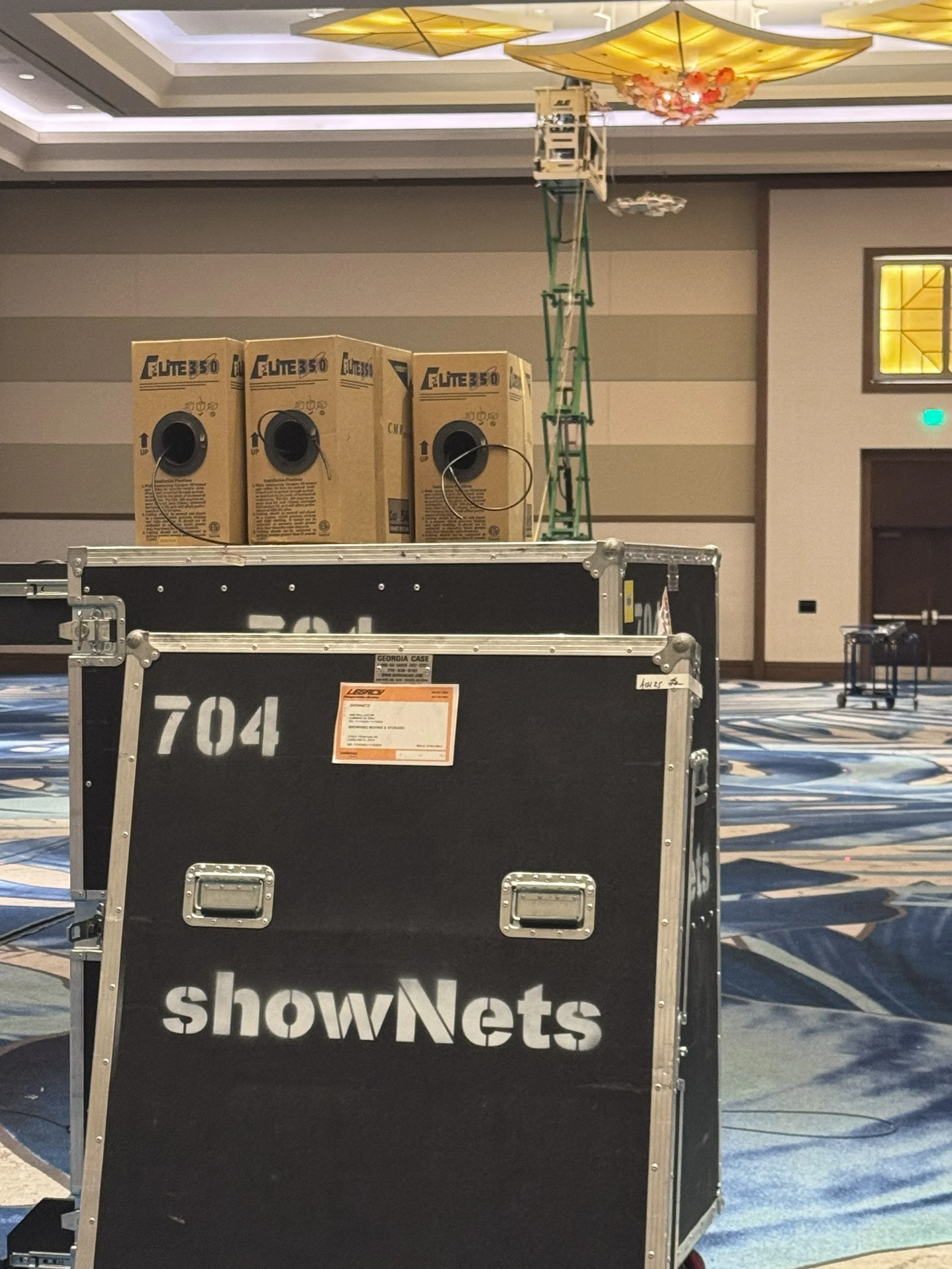 Empty conference or event space with showNets equipment boxes and a black flight case labeled showNets, a sign that says 'showNets', and some lighting and decorative ceiling fixtures.