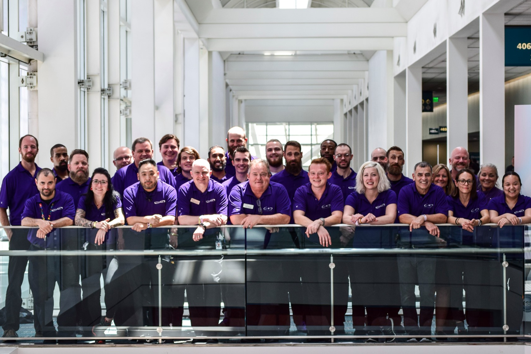 Group of diverse employees wearing matching purple shirts standing in a modern office building.