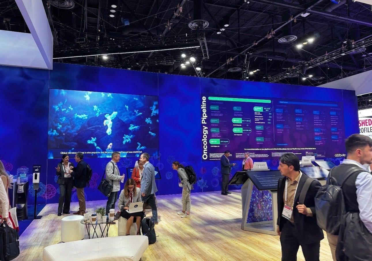 A large blue conference booth displaying information about oncology pipelines with attendees engaging in discussion at a medical or scientific event.