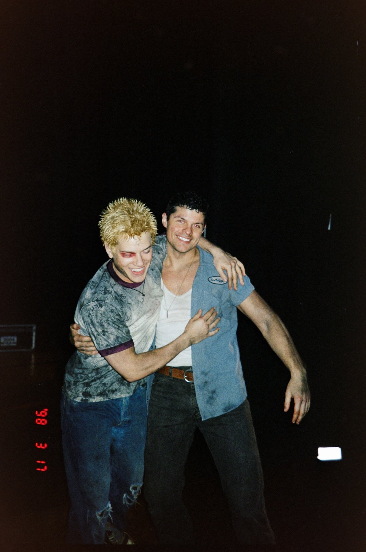 Two young men smiling and hugging each other at night outdoors.