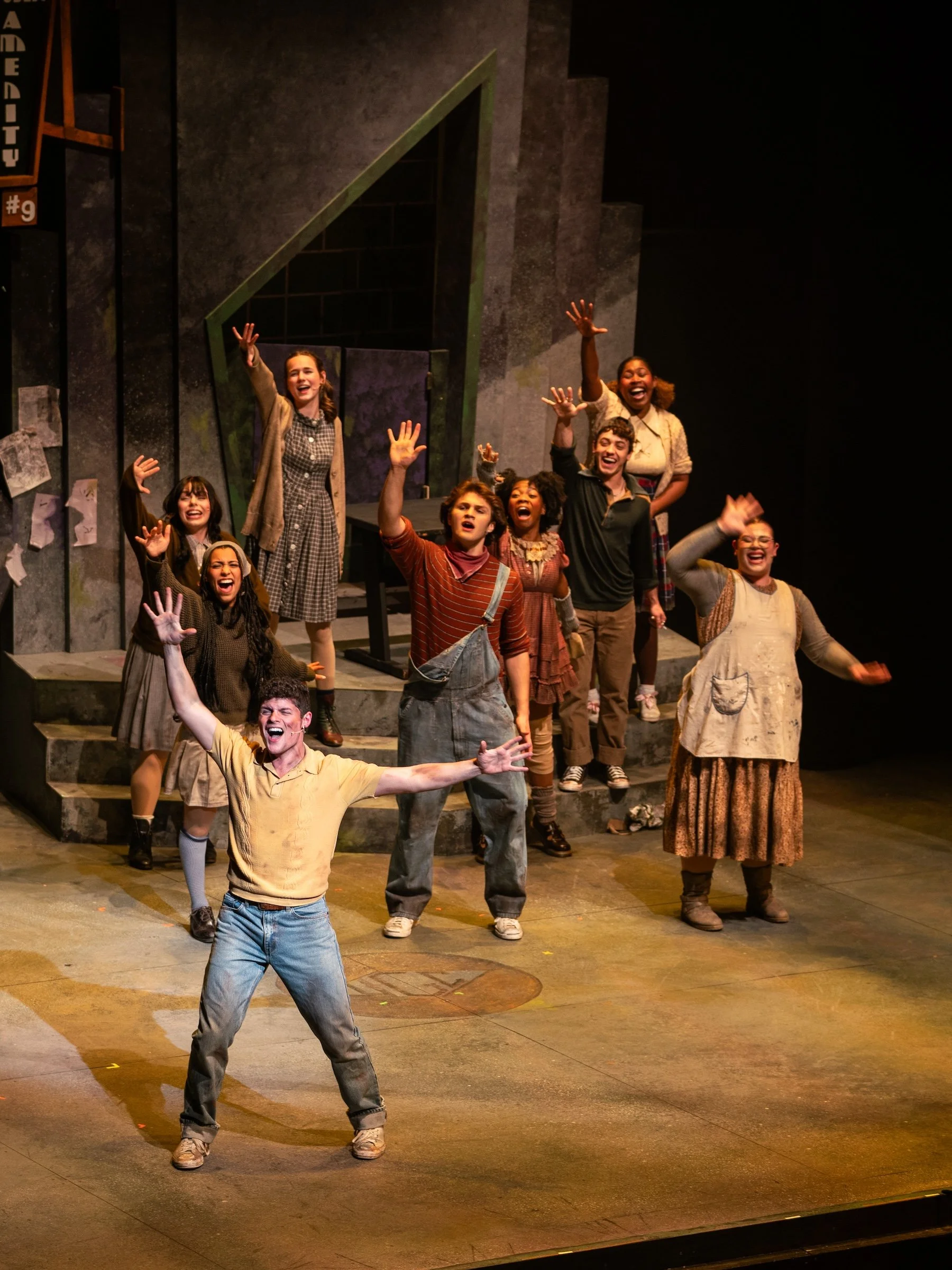 Group of diverse actors on stage, smiling and waving, during a theatrical performance.