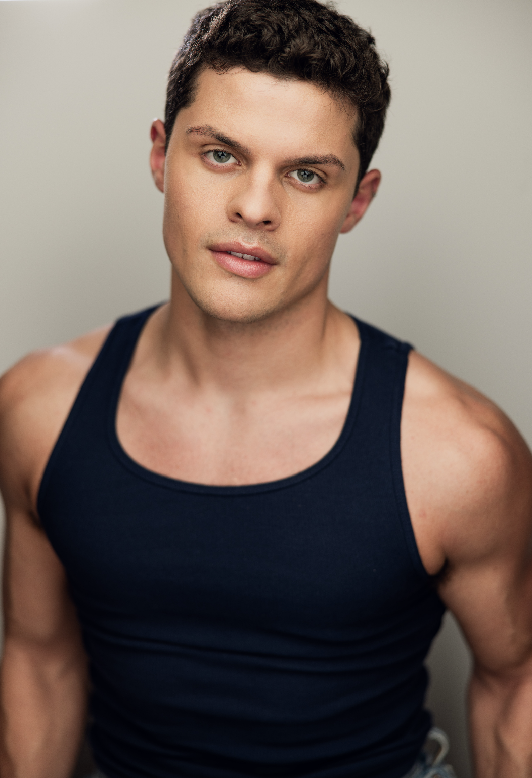 A young man with short dark hair and blue eyes wearing a black tank top, looking at the camera.