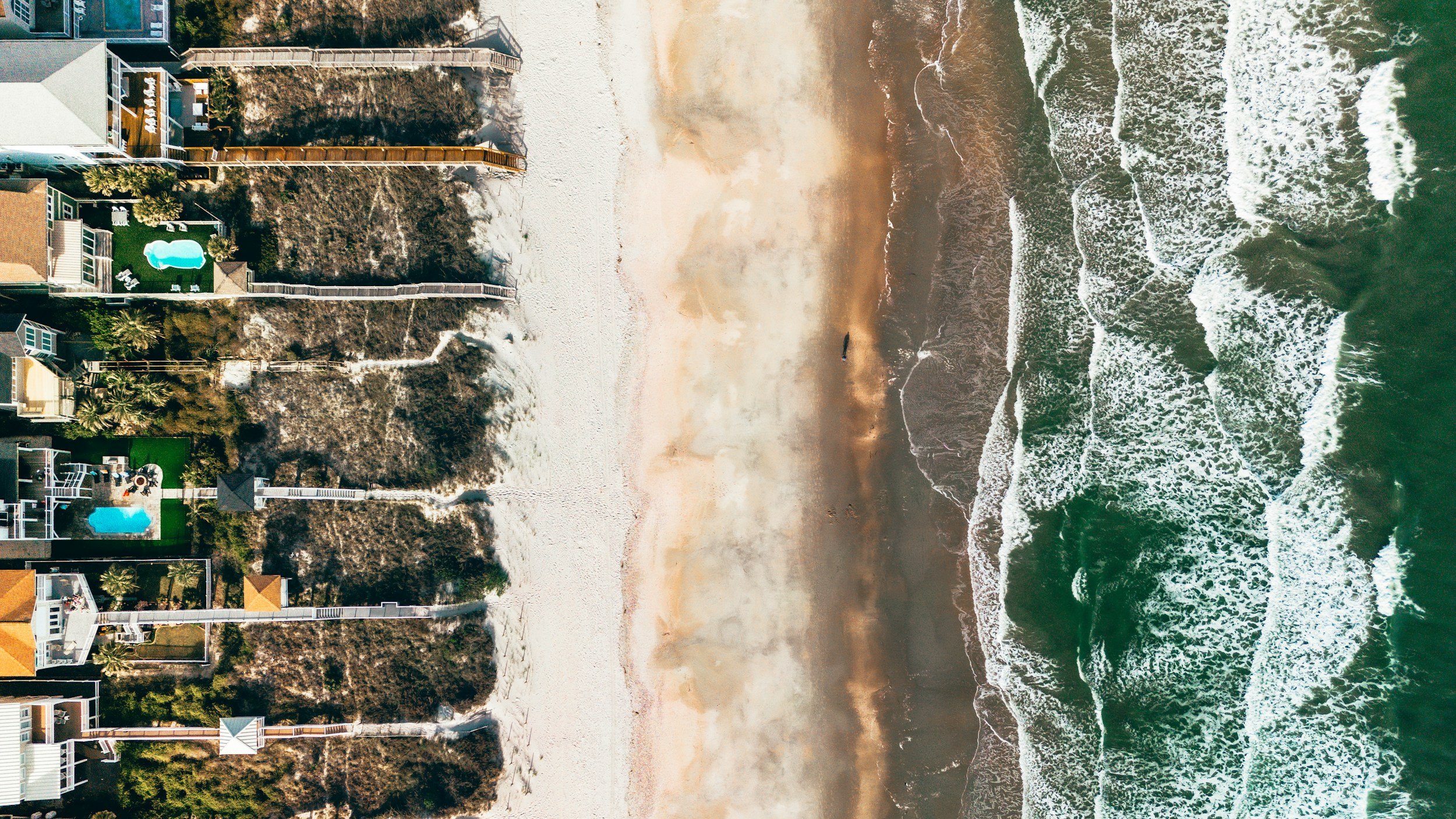 Aerial view of beachfront houses with pools, sandy beach, and ocean waves