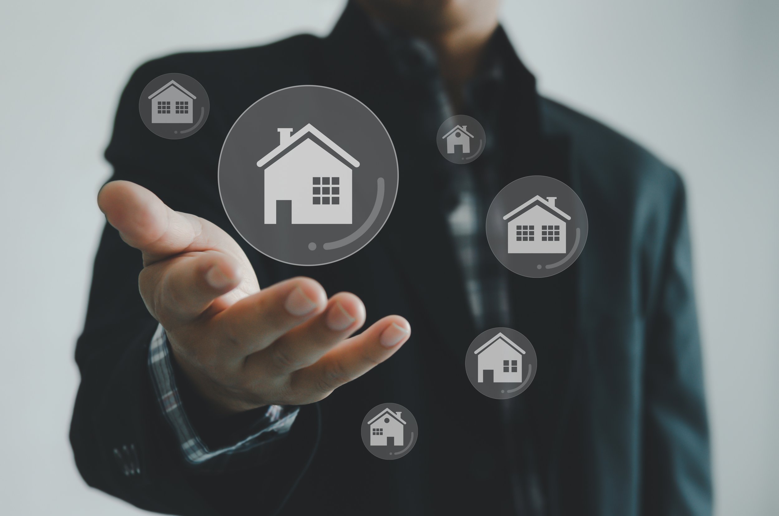 A person in a black suit points to virtual house icons displayed on a transparent screen, with only their torso visible.