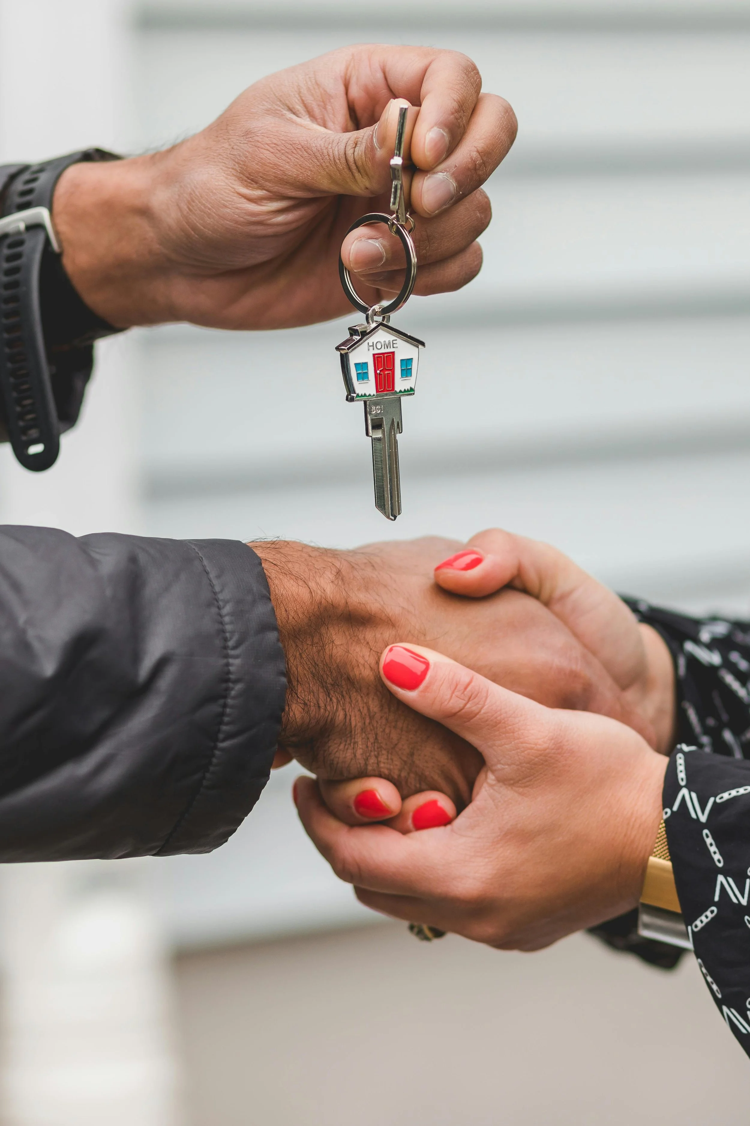 Two people are exchanging a house-shaped keychain with a key attached, representing handing over home ownership, while holding hands in a gesture of agreement.