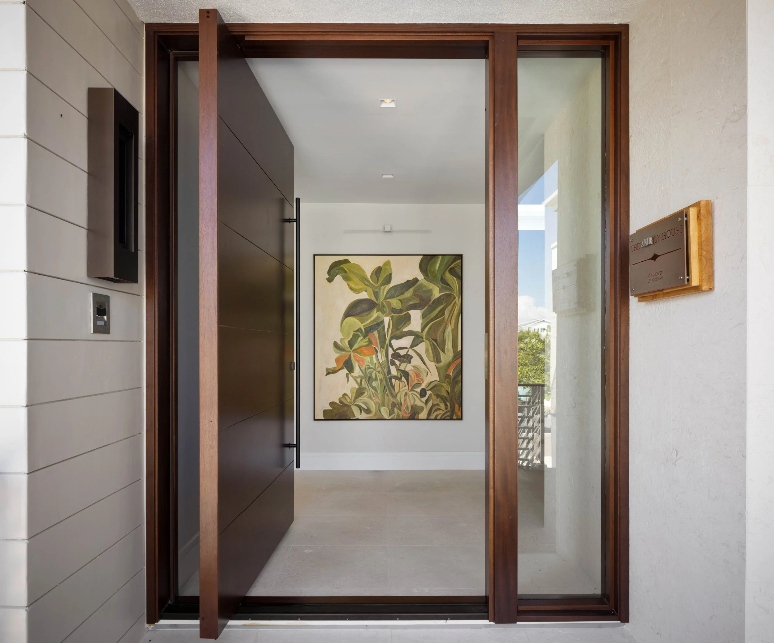 A modern house entryway with a sliding glass door, wood frame, and a decorative interior painting of green and orange leaves.