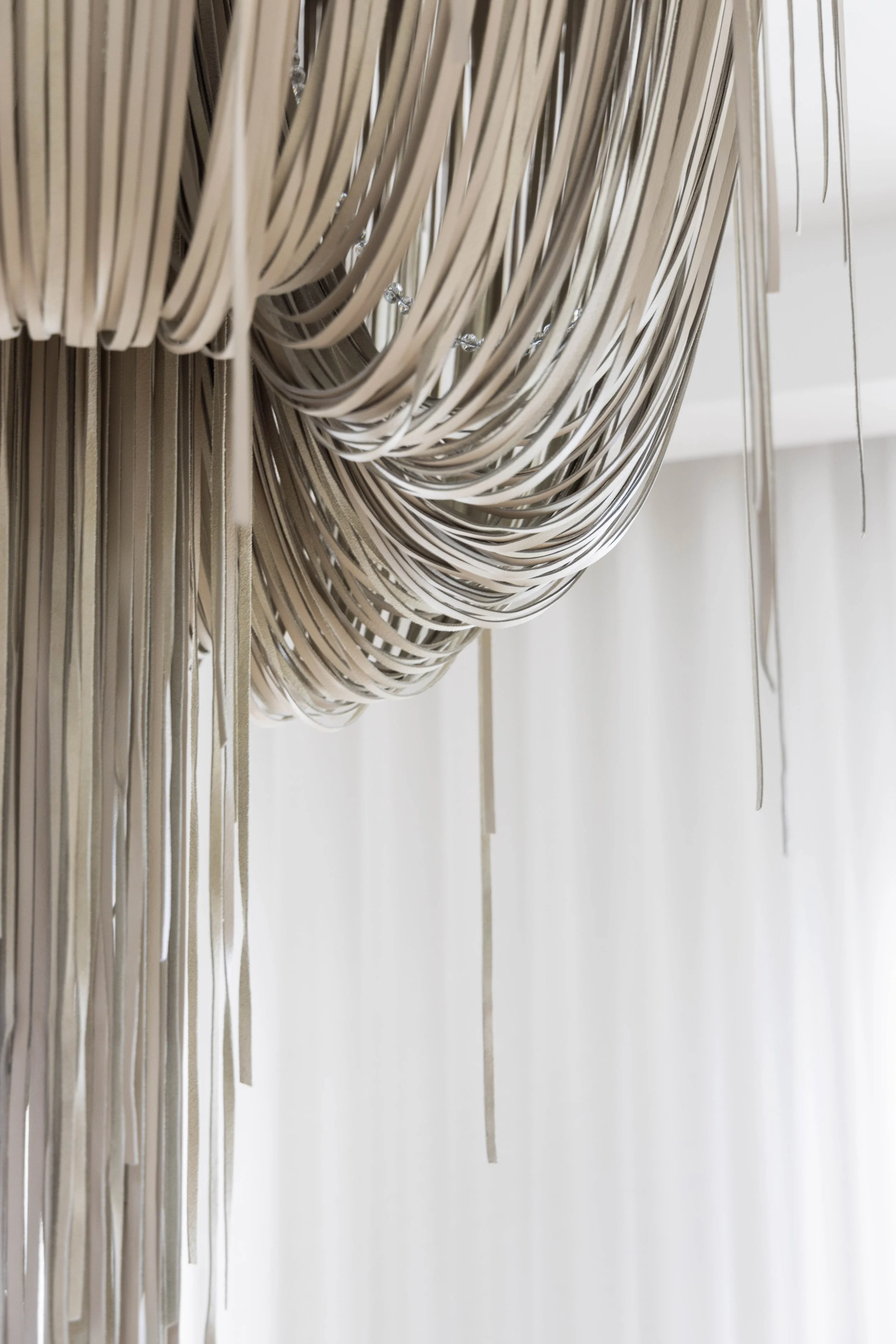 Close-up of a modern chandelier with multiple metal and crystal elements hanging against a white wall.