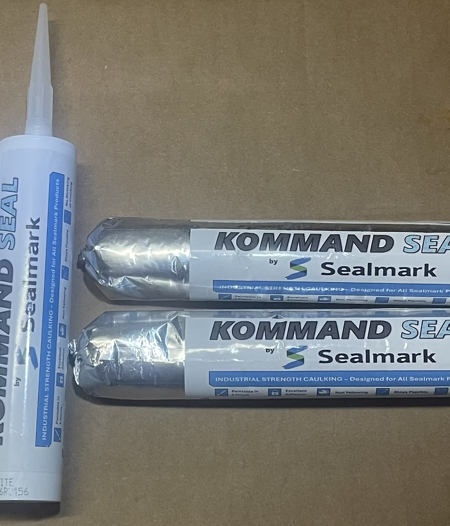 Three tubes of Sealmark Kommand Sealant on a surface, with one tube on the left and two tubes stacked horizontally on the right.
