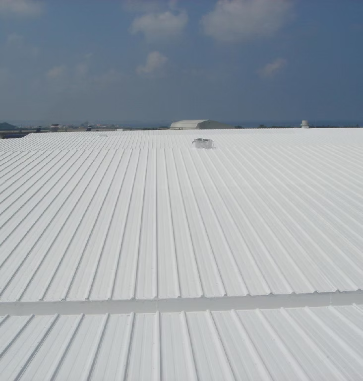 A white metal rooftop with a small vent, under a partly cloudy sky, with distant buildings visible in the background.