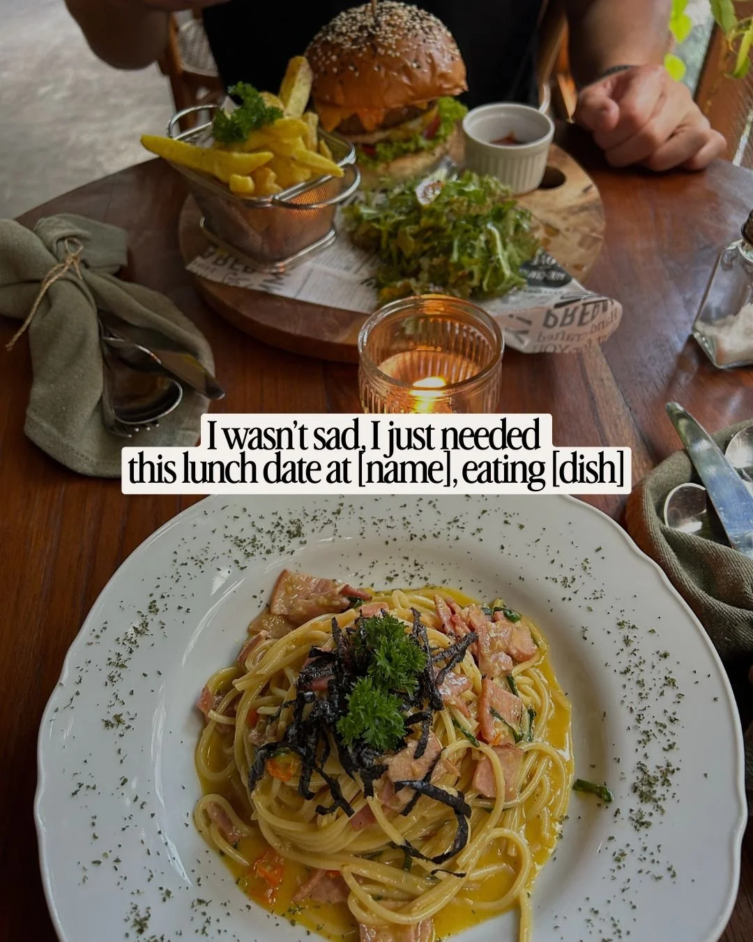 A plate of spaghetti with sliced ham, garnished with parsley and seaweed, on a white plate; in the background, a burger with fries, a small salad, and drinks on a wooden table, along with a lit candle.