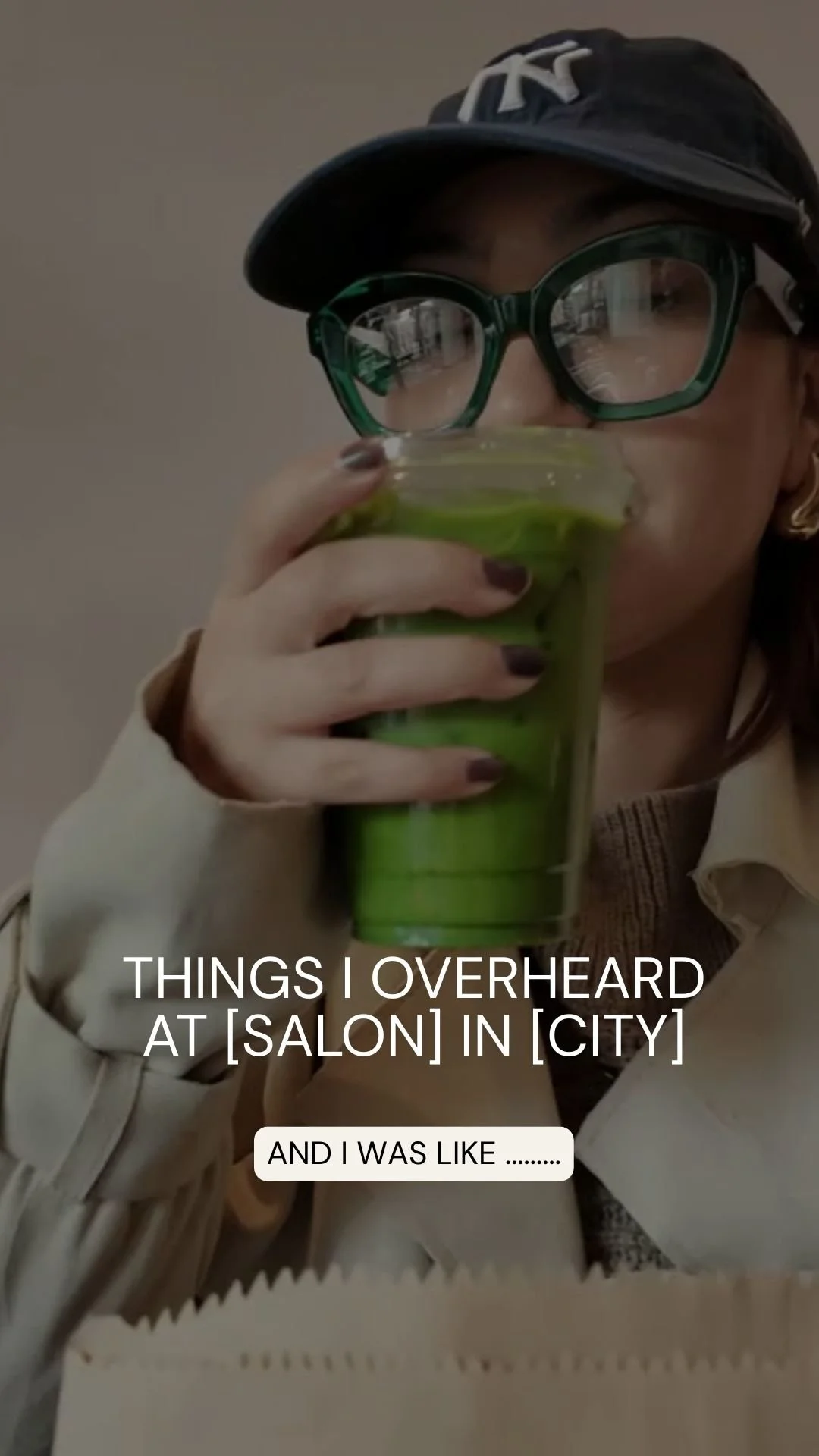 Person wearing black New York Yankees cap, large glasses, beige coat, drinking green beverage from a glass in a salon or cafe setting.