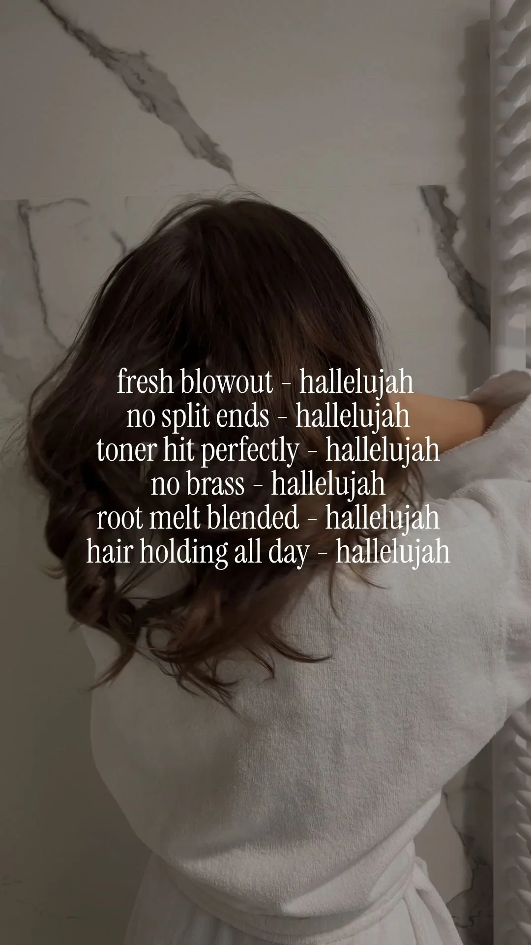 Woman with curled brown hair wrapped in a white robe, sitting in front of a marble wall with text overlay.