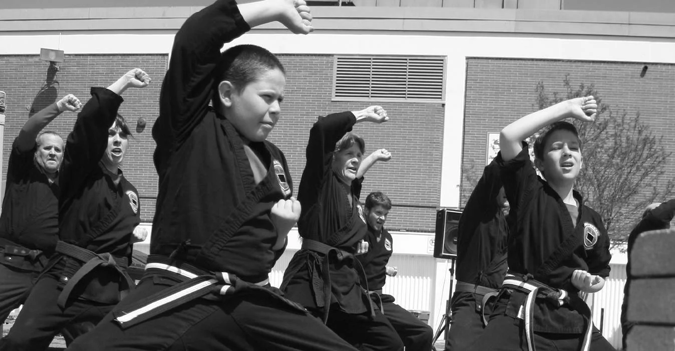 A class of karate students of varying age and skill level perform a blocking motion.