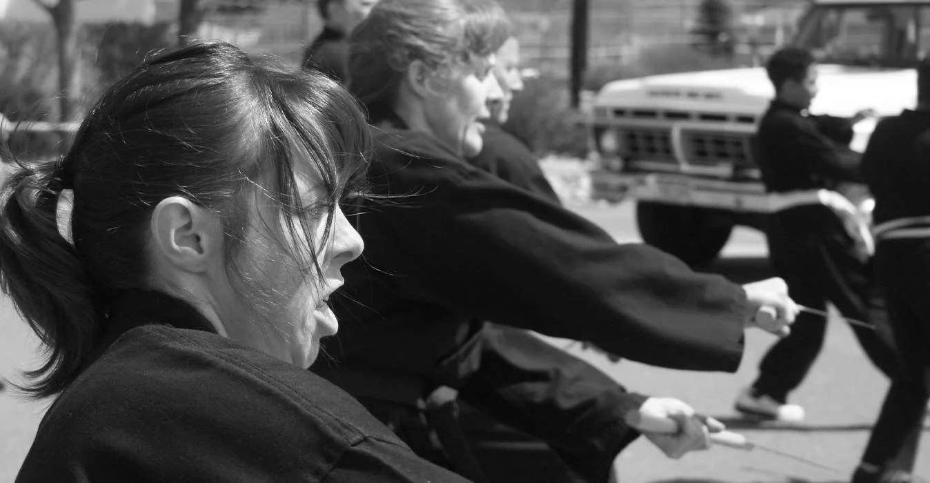 Adult students demonstrating martial arts outdoors in a line, focused on their movements.