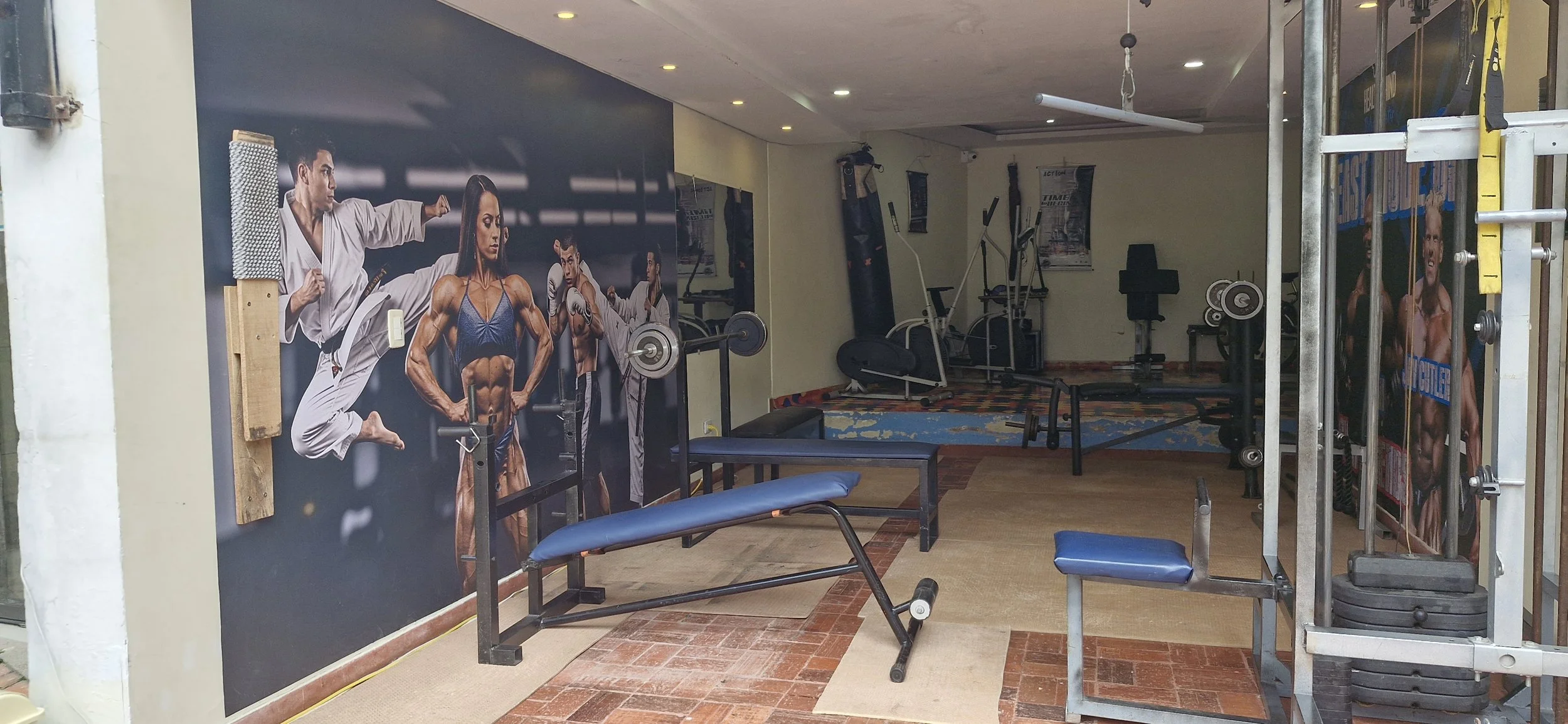 Gimnasio con equipos de entrenamiento, colchonetas y posters de culturismo en la pared