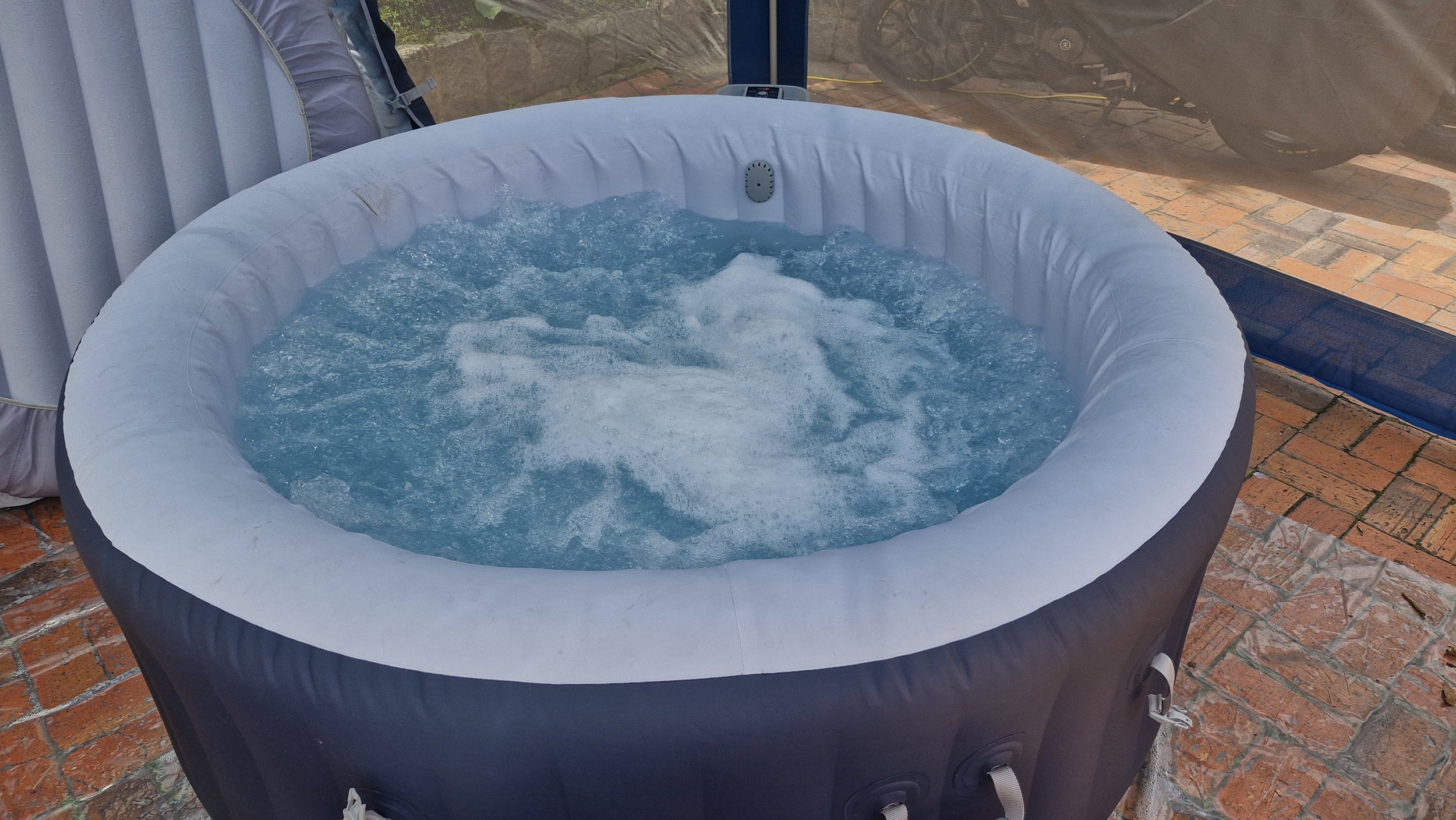 Jacuzzi inflable con agua burbujeante, en un espacio con paredes de ladrillo y una pared de cristal, exterior.