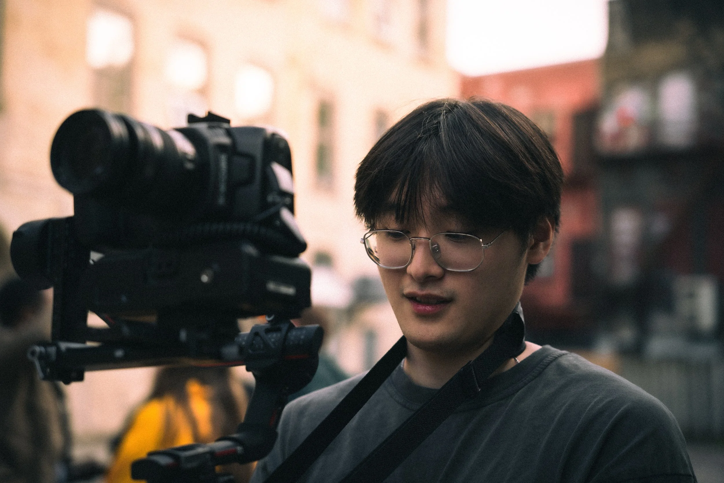 Young person with glasses looking at camera equipment outdoors. Videographer. Video producer. Cinematographer.