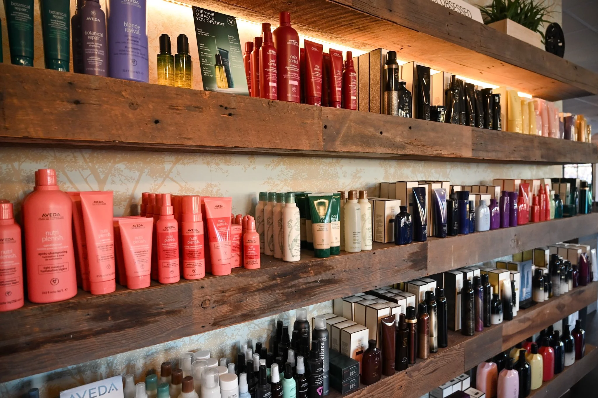 Wooden shelves displaying various hair care and beauty products, including bottles and tubes in different colors like pink, purple, black, and white, in a store.