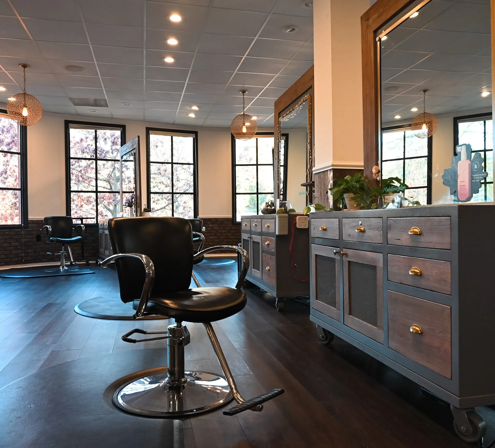 Interior of a modern salon with black chairs, large windows, wooden cabinets, and warm lighting.